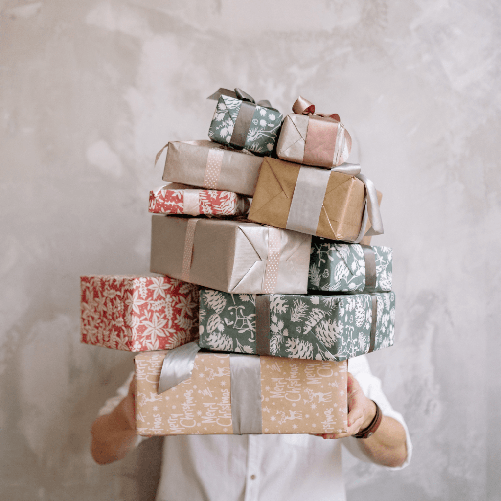 Person holding a pile of holiday gifts wrapped in reused gift wrapping